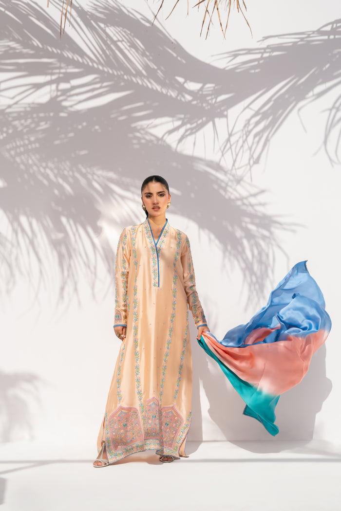 Woman in a long, light-colored dress holding a colorful fabric against a white background with palm leaf shadows.