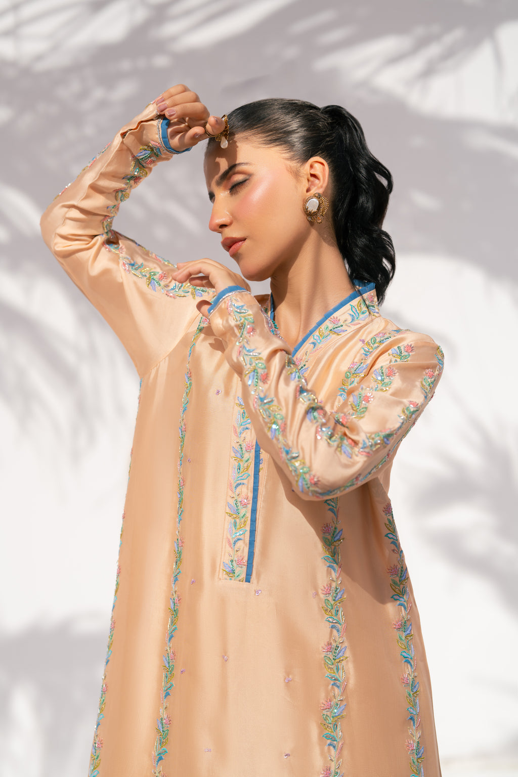 Woman wearing a peach-colored traditional outfit with floral embroidery against a white background