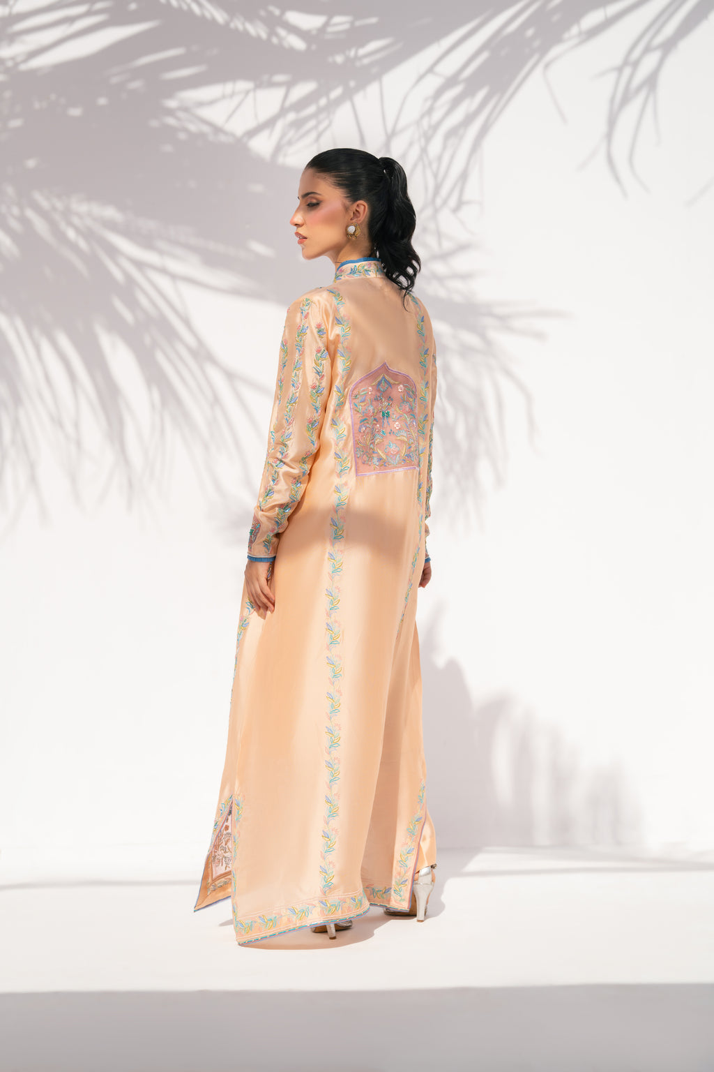 Woman wearing a peach embroidered traditional outfit against a white background