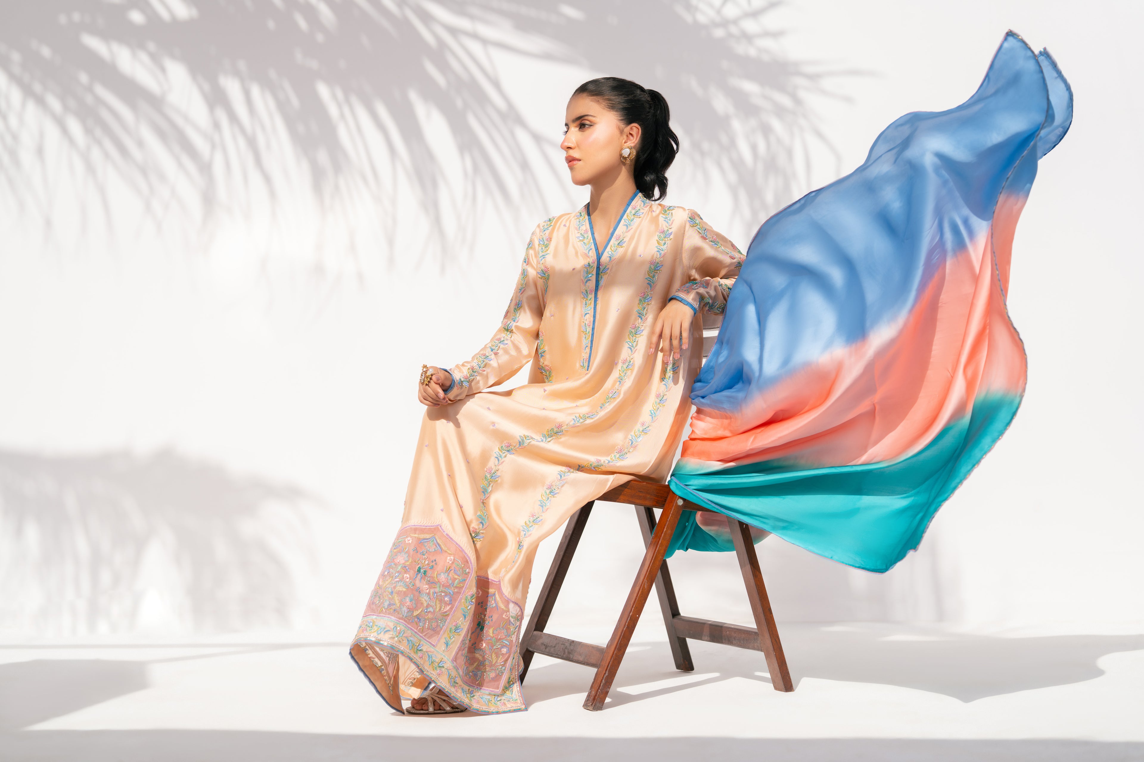 Woman in a traditional outfit with a colorful fabric draped over a chair on a white background