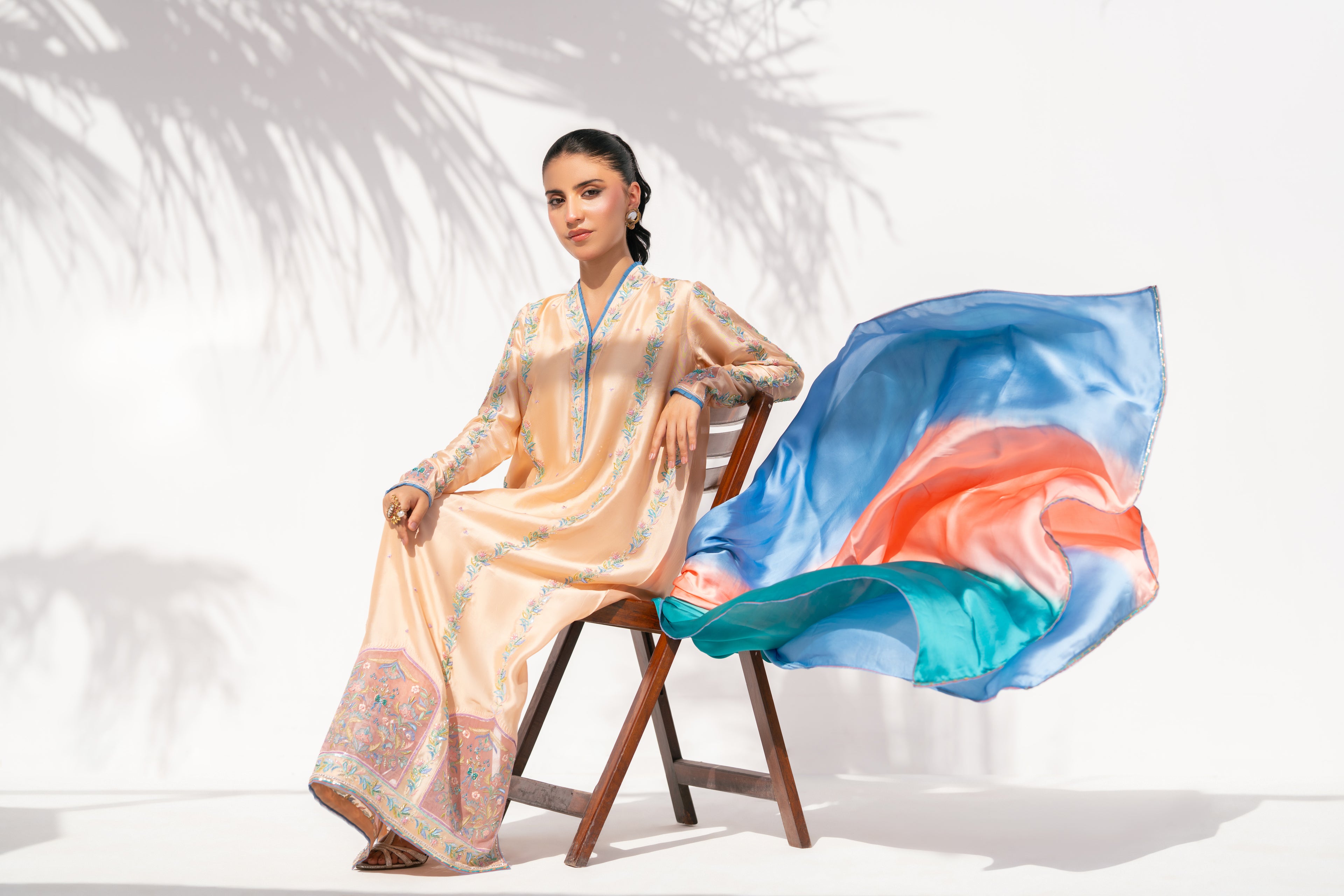 Woman in a peach-colored traditional outfit with a flowing fabric on a white background