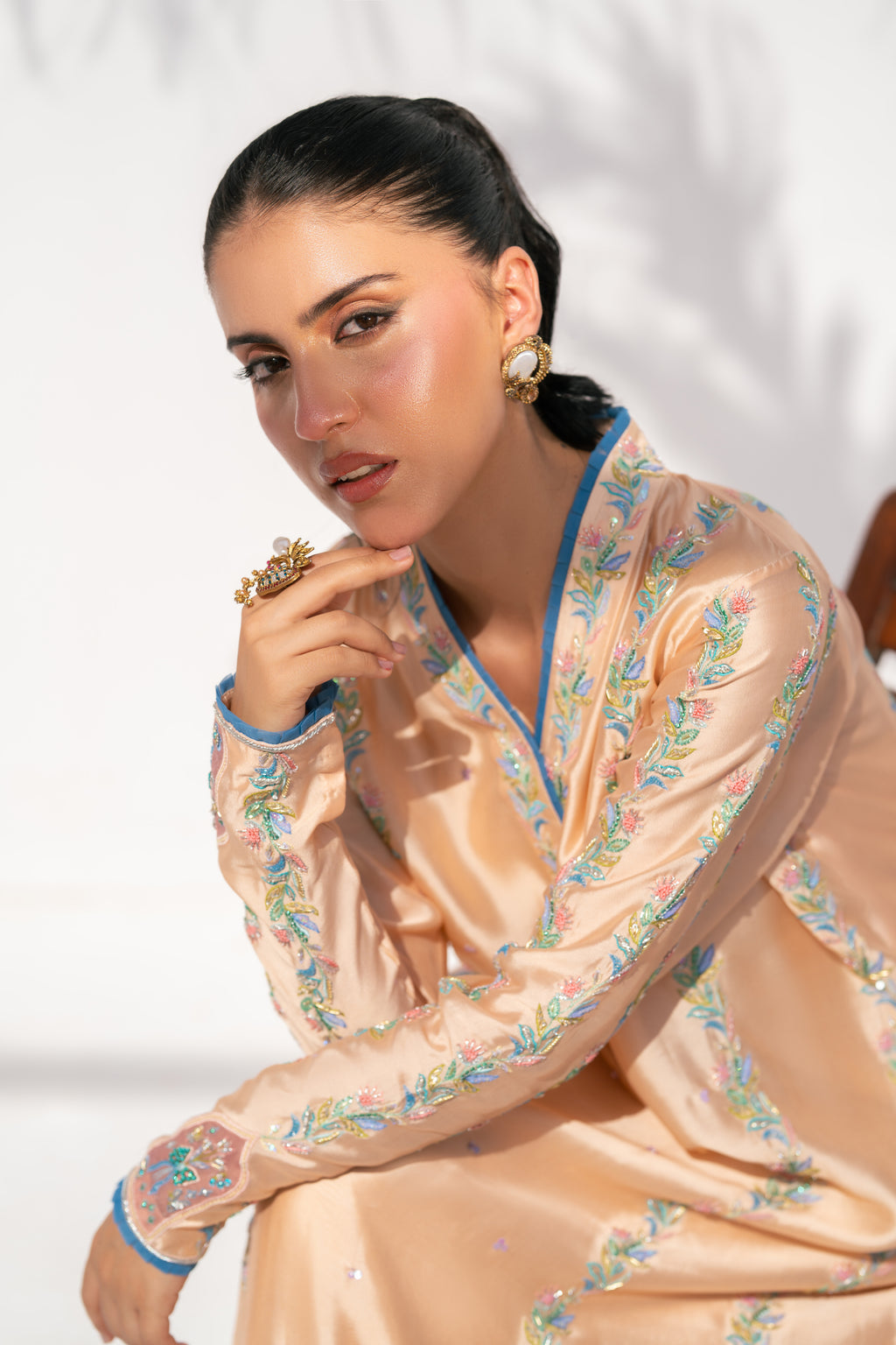 Woman wearing a peach embroidered traditional outfit against a white background