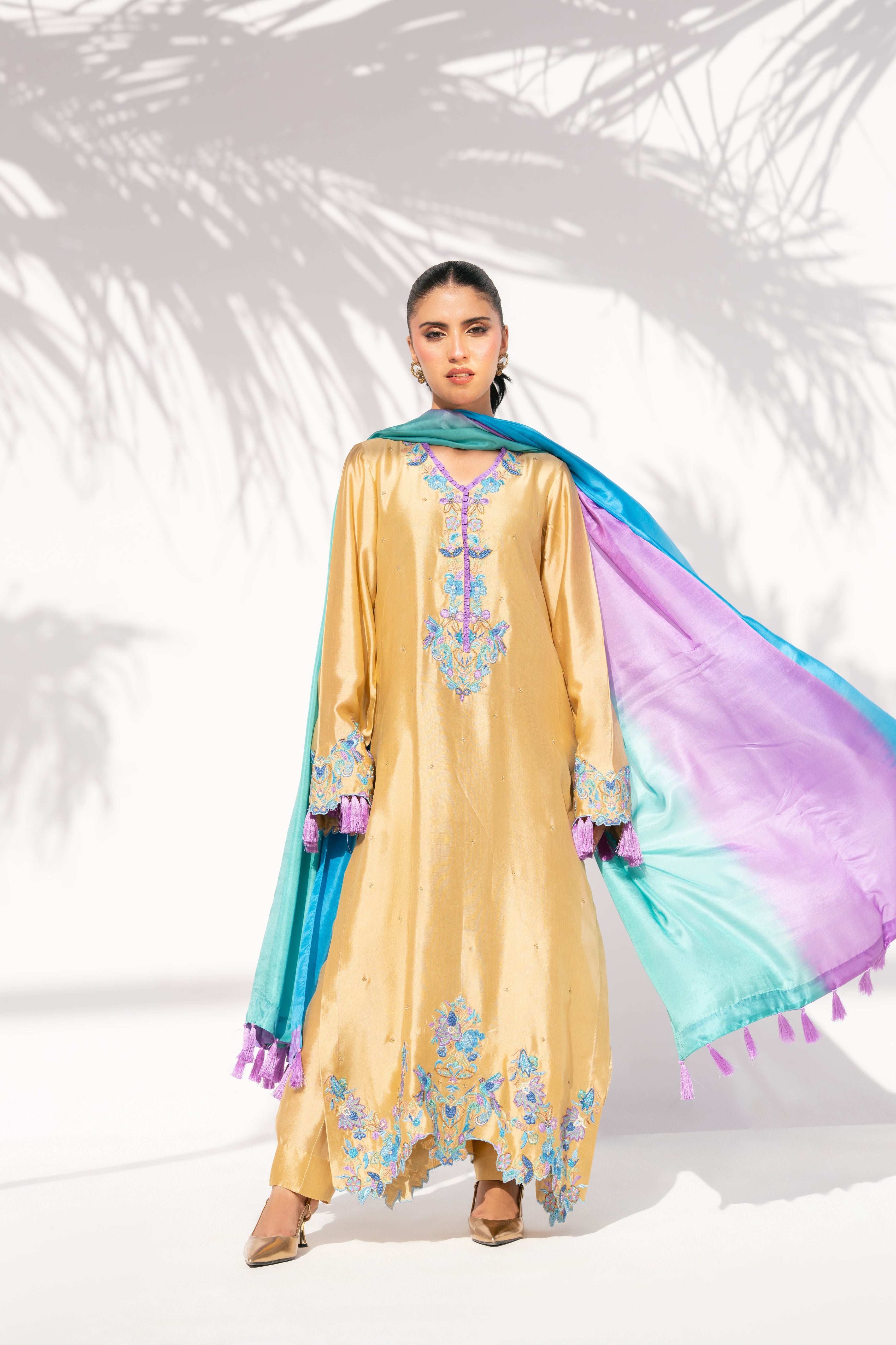 Woman wearing a beige embroidered dress with colorful dupatta against a white background