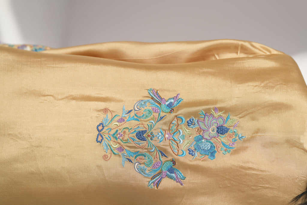 Gold fabric with intricate blue and green floral embroidery on a plain background