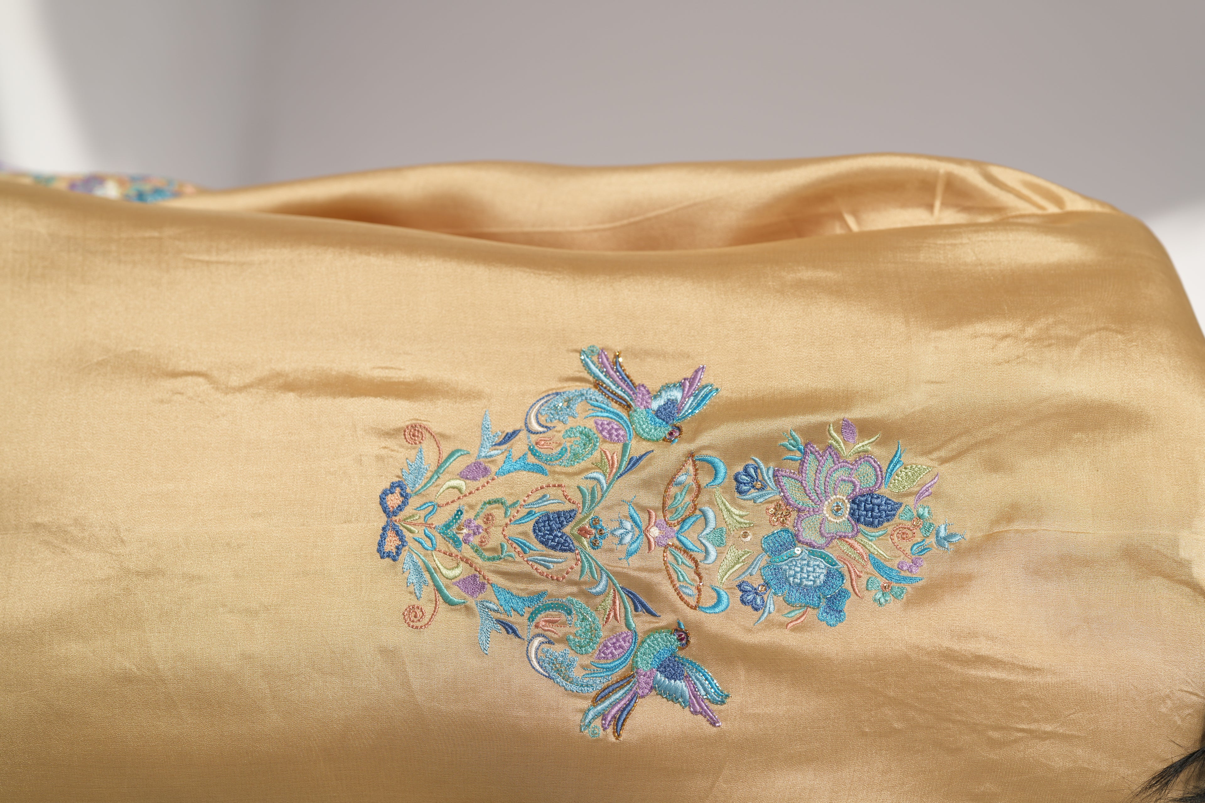 Gold fabric with intricate blue and green floral embroidery on a plain background